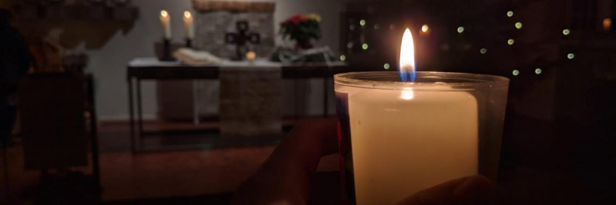 Blick über eine Kerze auf den Altarraum mit Adventskranz und Weihnachtsbaum
